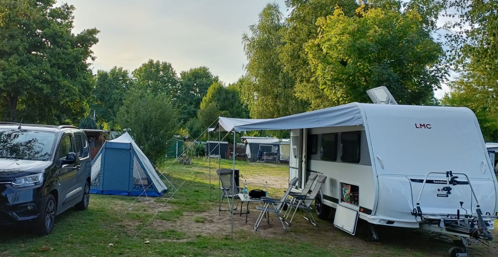 Camping mit Wohnwagen und Zelt, Aufgebaut auf dem Campingplatz mit Vorzelt und Auto auf der Parzelle