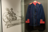 Quelle: Museum Erding, Eine Wollweberin an einem Spinnrad französischer Bauart, daneben Uniformjacke aus Loden des Vaters des berühmten Erdinger Tiermalers Franz Xaver Stahl